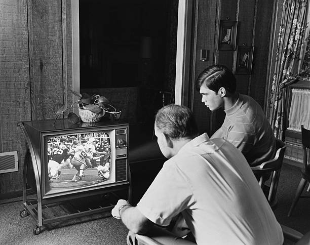 1960s 1970s TEEN BOY WATCHING FOOTBALL GAME ON TELEVISION WITH ADULT DAD